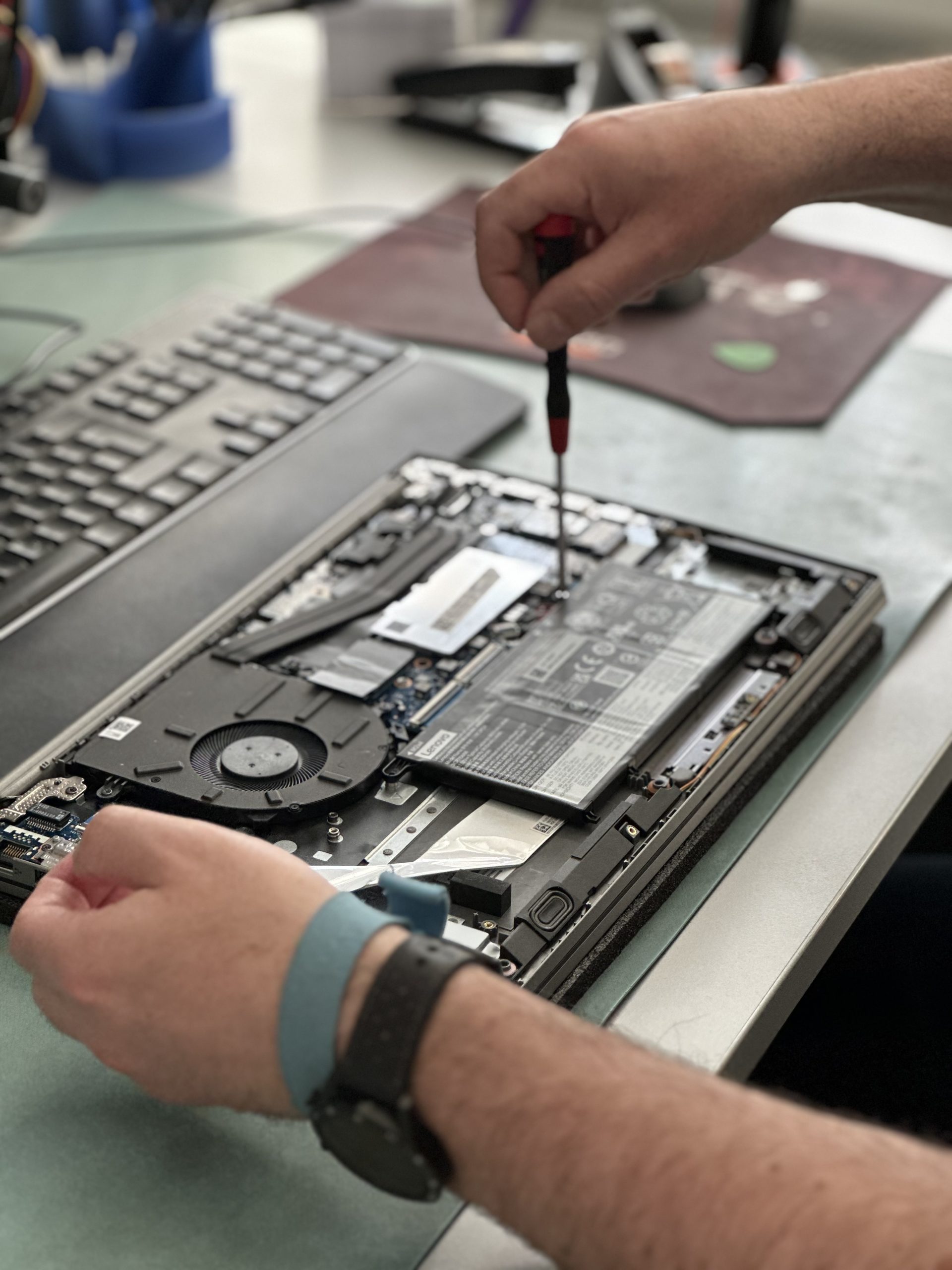 Ein Techniker repariert ein Notebook auf einer ESD-Matte, während er ein Erdungsarmband um das Handgelenk trägt. Diese Sicherheitsvorkehrung schützt das Gerät vor elektrostatischen Entladungen, was die präzise und sichere Durchführung der Reparatur gewährleistet.