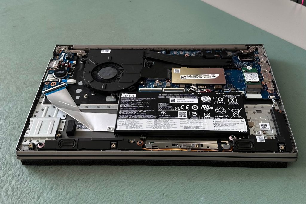 Ein Notebook liegt auf einer grünen ESD-Matte, mit der Rückseite geöffnet und sichtbar. Die ESD-Matte schützt das Gerät vor elektrostatischen Entladungen, während der Techniker an den internen Komponenten arbeitet.